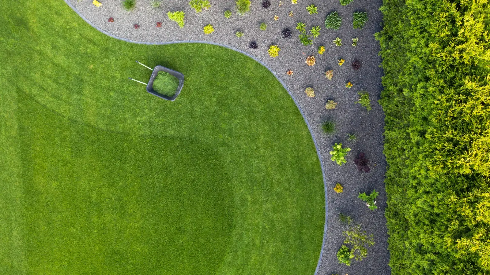 aerial view of a neatly maintained lawn with curved edging, a gravel garden bed, and a wheelbarrow filled with grass clippings
