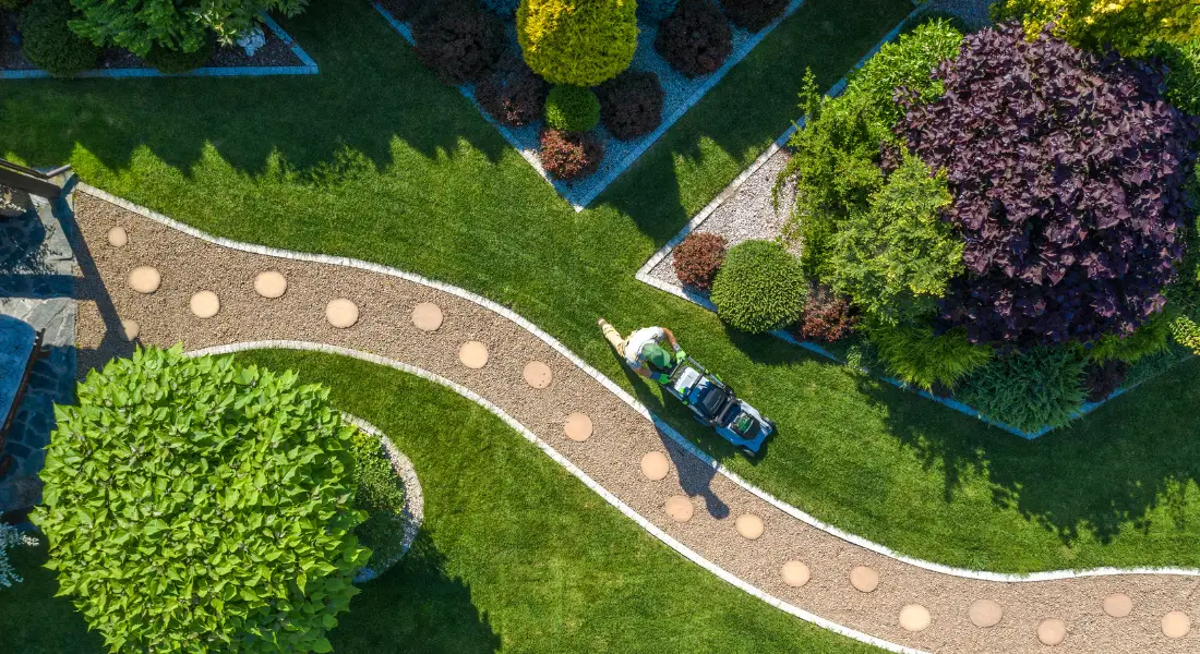 aerial view of a person mowing a well landscaped backyard with winding gravel paths and manicured shrubs