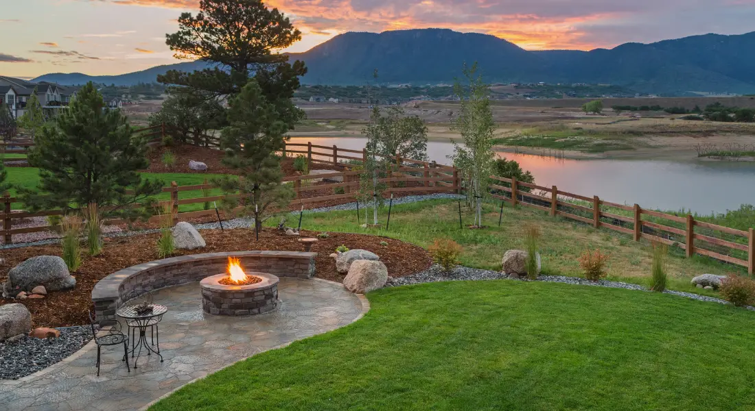 backyard fire pit with stone patio overlooking lake and mountains at sunset