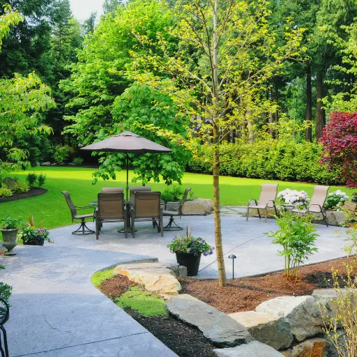 backyard patio with outdoor seating, umbrella, and landscaped garden surrounded by trees