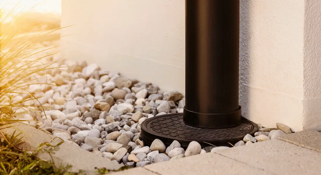 close up of a downspout drainage system surrounded by decorative stones.