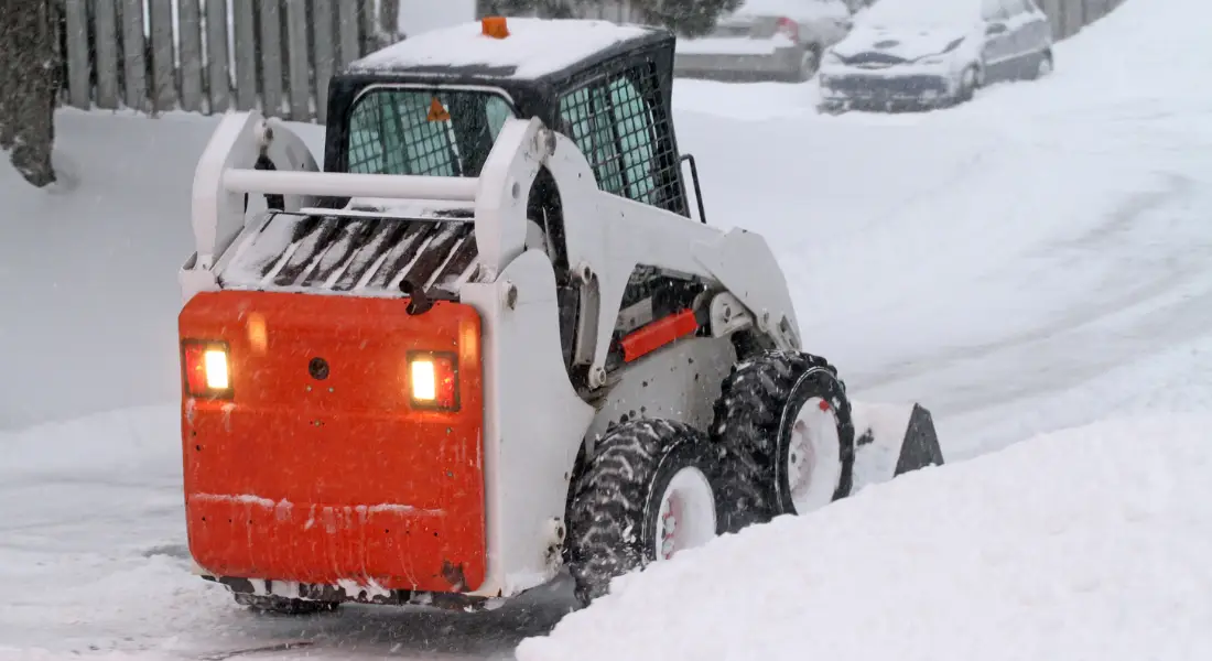 compact snow plow clearing a residential street during heavy snowfall