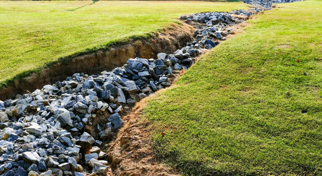 grassy yard with a drainage ditch filled with large rocks for erosion control
