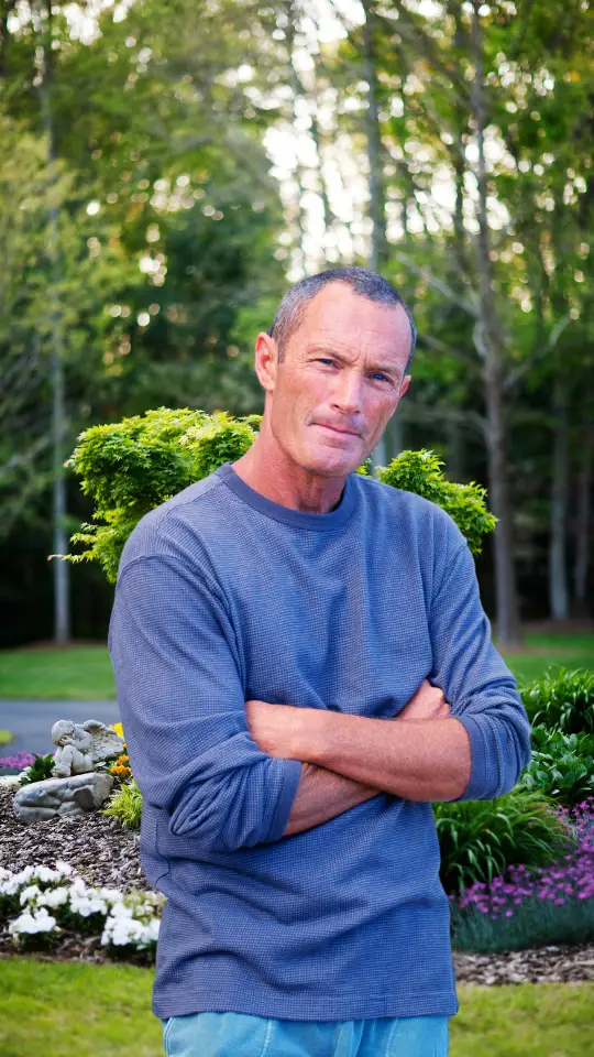 man standing confidently in a landscaped garden with arms crossed