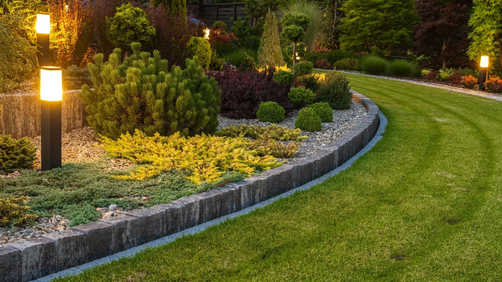 well lit landscaped garden at dusk with decorative plants, edging stones, and modern outdoor path lights