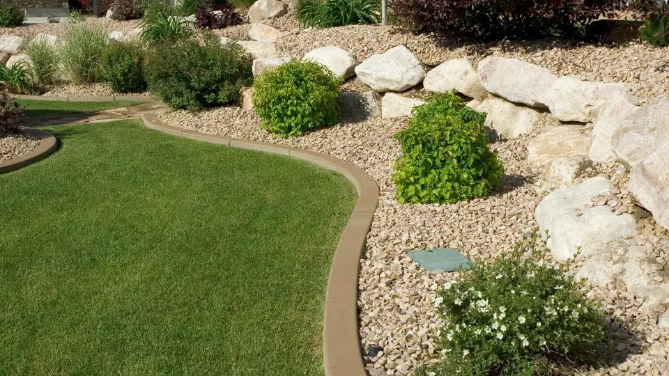 well maintained backyard with curved lawn edge, decorative rocks, shrubs, and stone retaining wall